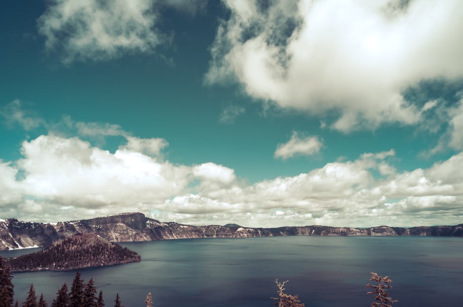 Breathtaking view of a serene mountain lake with lush landscape under a vast cloudy sky.