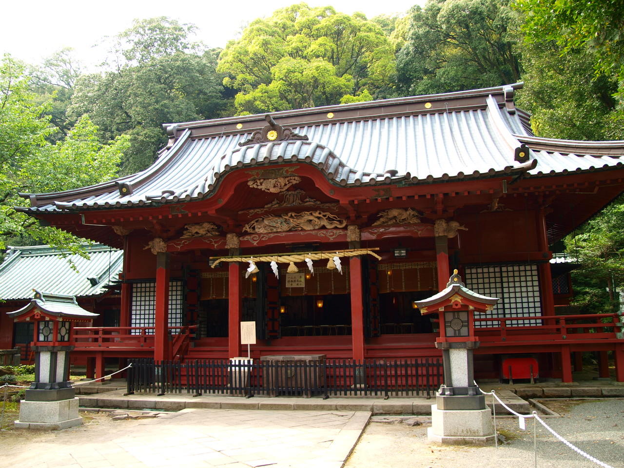The vermilion main hall of Izusan Shrine with dragon carvings, surrounded by green forest