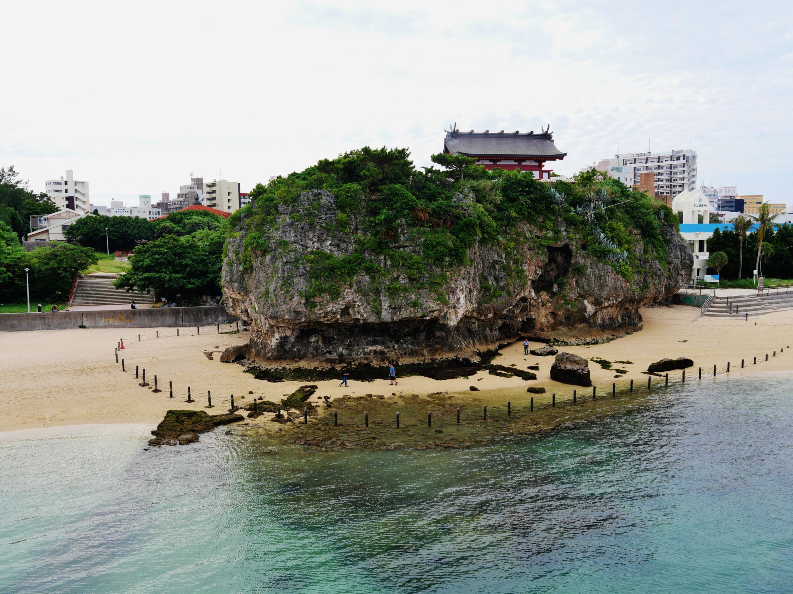 Naminoue Shrine on its cliff above Naminoue Beach, with turquoise ocean water in the foreground